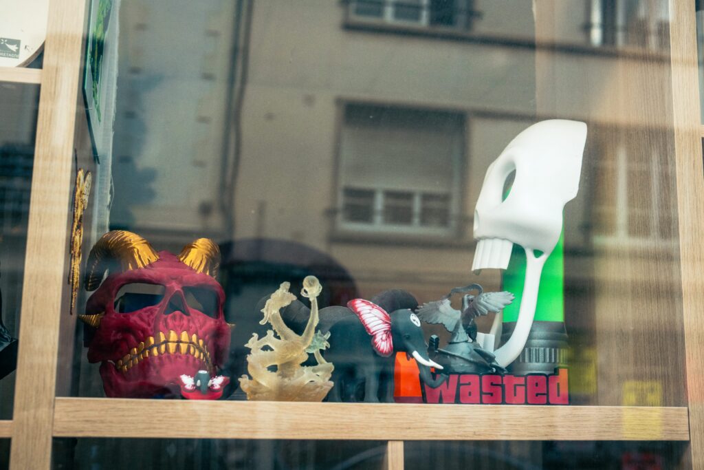 Vitrine de Hephaprint présentant des figurines et masques imprimés en 3D, dont un crâne de démon rouge et un masque blanc.